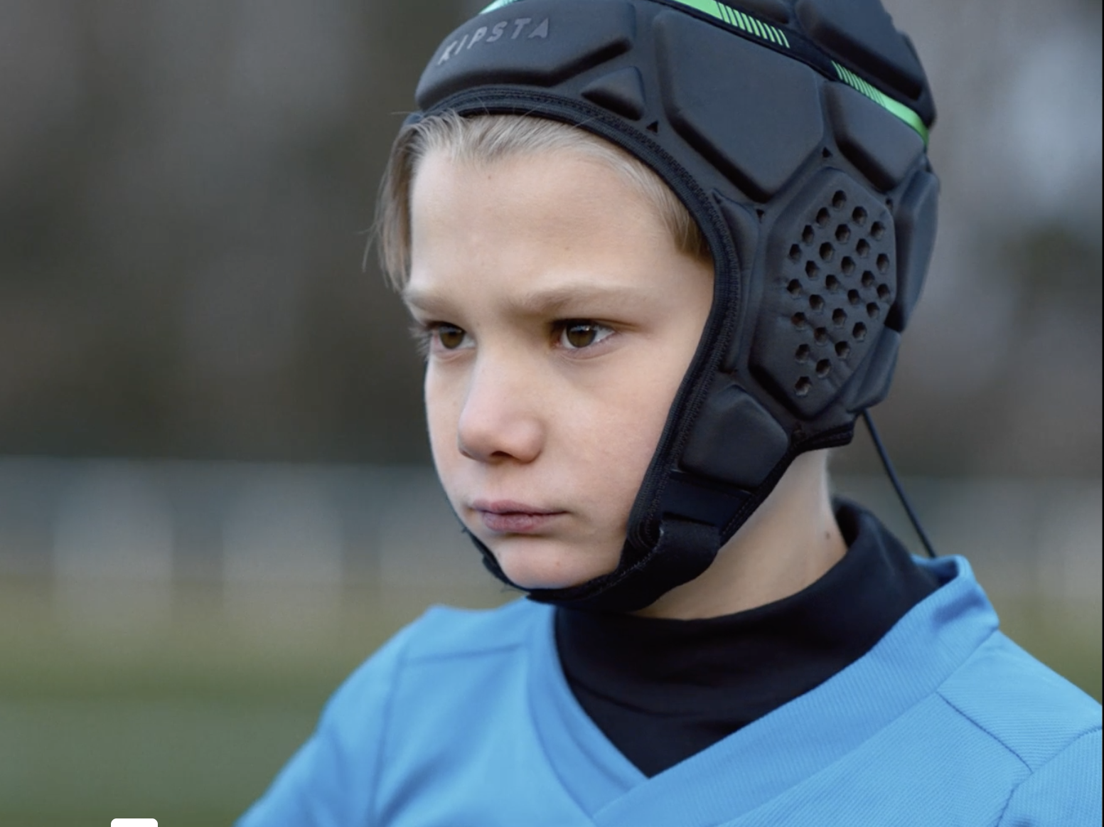 un petit garçon, visage fermé, casque de rugby sur la tête